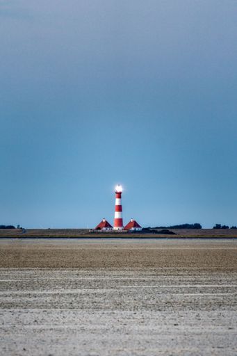 A vertical shot of a field with a lighthouse in the background on a  sunny day