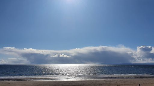 A mesmerizing cloudscape over a sea with shiny water and sandy coast