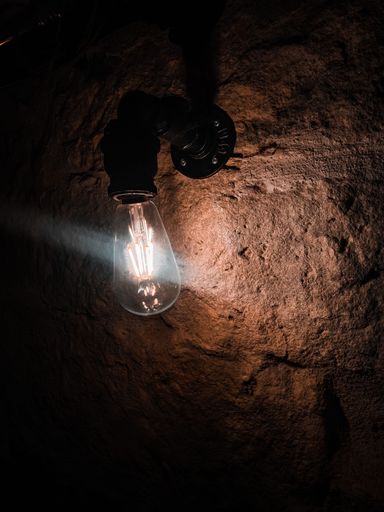 A vertical closeup shot of an illuminated old lightbulb in a stone tunnel