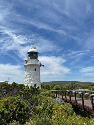 A vertical shot of a white beacon on a cliff near a bridge under blue cloudy sky