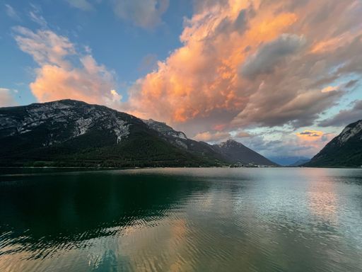 A scenic shot of a lake surrounded by mountains under a cloudy sunset sky