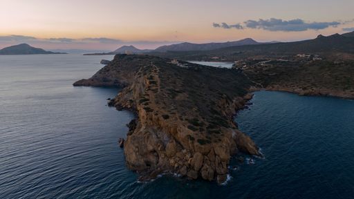 A bird's eye view of a coastal cliff surrounded by water seen during the sunset