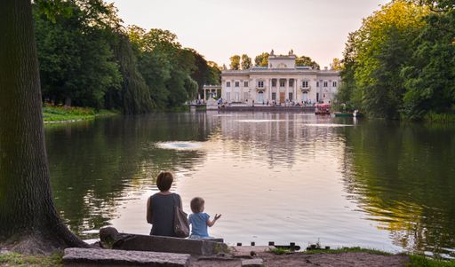 A woman with her daughter sitting on the lakeside and looking at Palace on the Isle. Warsaw, Poland.