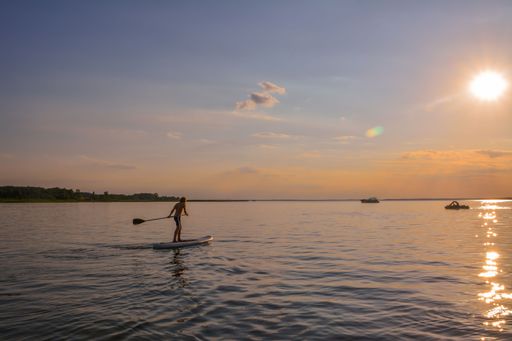A scenic view of a young boy rowing on a paddleboat with the sun setting in the background