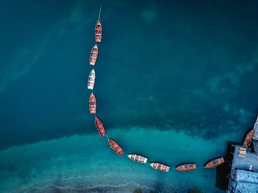 An aerial top view of sailing boats moored to each other in a curvy line in a turquoise sea