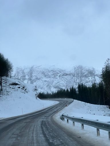 A narrow country ice road between snowy  Norwegian mountains in the winter, vertical shot