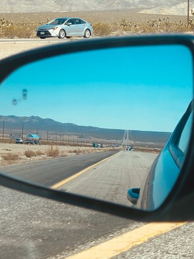 A vertical shot of a road and a vast landscape is seen from a car's side mirror
