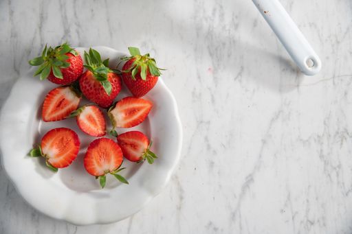 A top view of a bowl with juicy red strawberries on a white marble table