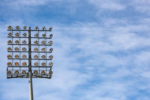 A low angle shot of a tall pole with stadium lights under a blue sky