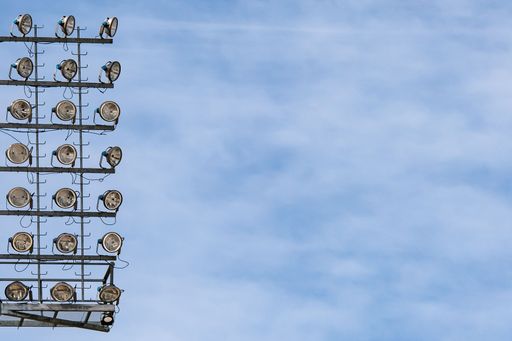 A low angle shot of a tall pole with stadium lights under a blue sky