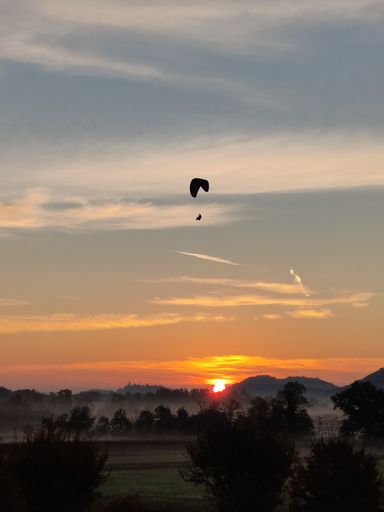 A scenic shot of paragliding flight over green valley during sunset