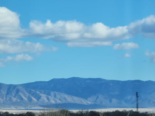 A beautiful landscape of high mountains, agricultural field next to green forest under blue cloudy sky