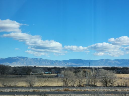 A beautiful landscape of high mountains, agricultural field next to green forest under blue cloudy sky