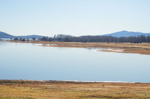 A scenic shot of the coast of a lake surrounded by hills under the blue sky