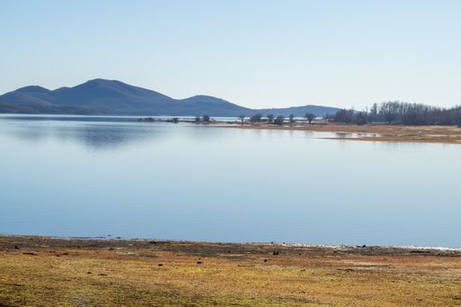 A scenic shot of the coast of a lake surrounded by hills under the blue sky