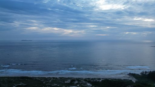 A landscape of a beach surrounded by the sea under a cloudy sky on a rainy day