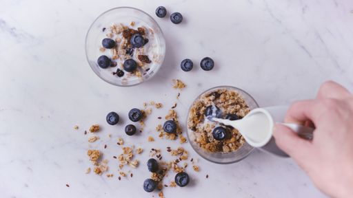 An overhead shot of a person pouring milk on natural breakfast with cereals and blueberries