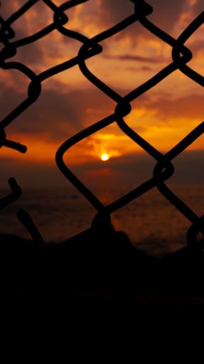 A scenic vivid sunset over the sea captured through a mesh fence