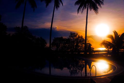 A scenic view of an orange sunset over Palawan bay reflected on the pool with palms in the Philippines