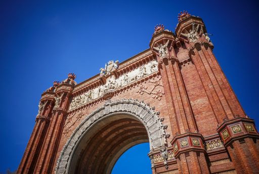A low angle shot of the historic Arc de Triomphe against a blue sky in Barcelona, Spain