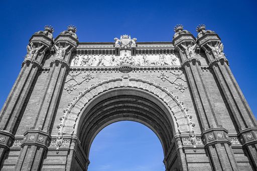 A low angle shot of the historic Arc de Triomphe against a blue sky in Barcelona, Spain