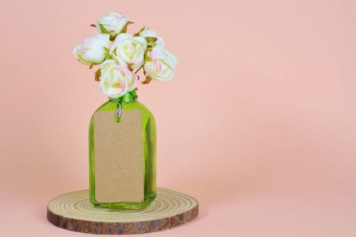A closeup shot of a glass container with a small bouquet of fabric roses in a plain background