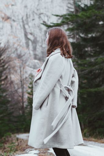 A vertical shot of the female from behind standing in the forest with trees