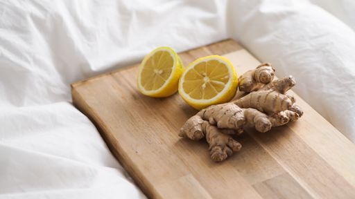 A wooden board with cut lemon and ginger roots on the white sheets