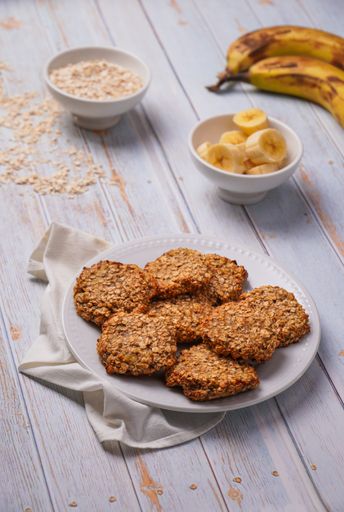 A vertical closeup shot of oatmeal banana cookies and ingredients on a wooden table