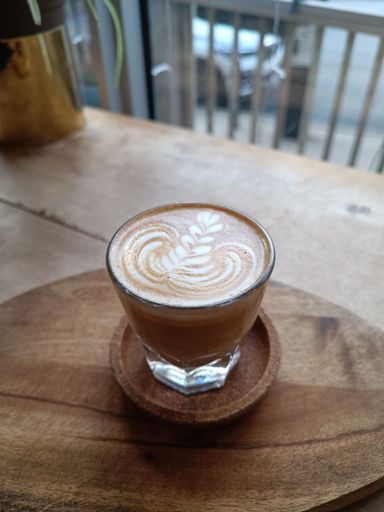 A vertical high angle shot of a cup a of cappuccino, with art on the foam, on a wooden plate