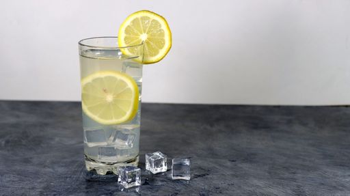 A glass with a gin lemon cocktail and icecubes on a gray table