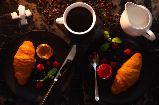 A top view of a black coffee on the table with two plates of croissants with jam