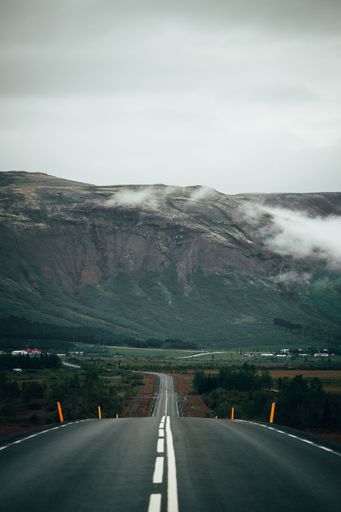 This stock photo features a view of an empty road winding through the mountains on a cloudy day