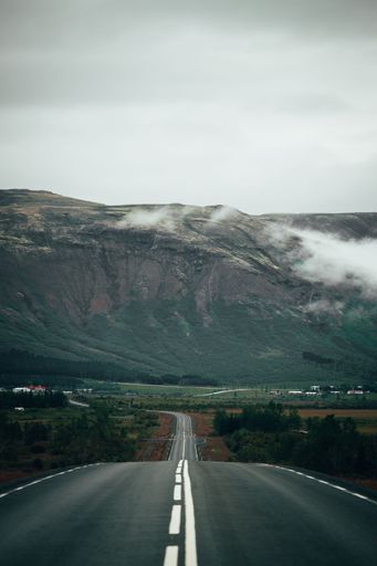 A scenic view of a winding road in the countryside, leading to a distant mountain range on the horizon