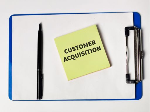 The words Customer Acquisition written on sticky notes with a pen and paper board.