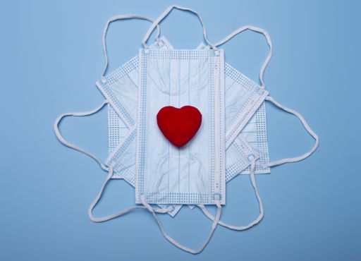 A top view of valentine composition of small red heart on face masks isolated on blue background - new normal concept