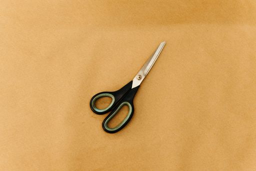 A pair of scissors laying on top of a sheet of brown paper on a flat surface