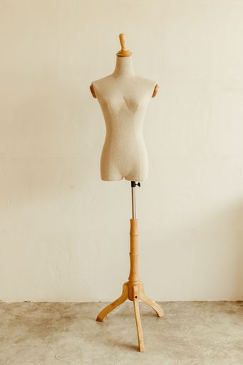 An isolated, white sewing mannequin is prominently displayed against a solid, neutral background in an empty room