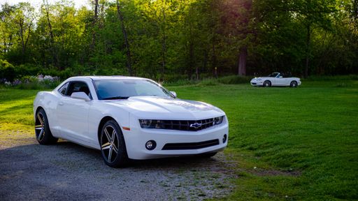 A closeup shot of a white Chevy Camaro and Mazda Miata in a park on a sunny day