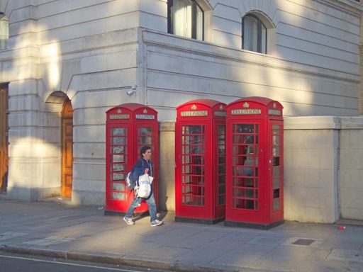 A man walks past three old traditional red British telephone boxes in Portland Place, London, United Kingdom. This type of phone box is becoming rare.