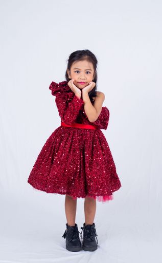 A young girl in a glittery red dress and black boots posing on the white background