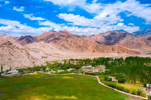 A scenic view of mountains ranges and plantations under the blue sky with clouds