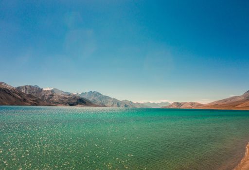 A scenic view of a turquoise sparkling sea with mountain ranges on the coastline on a sunny day