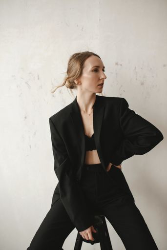 A beautiful young European girl in a black suit posing at the camera while sitting on a stool