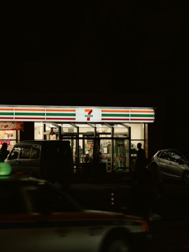 An illuminated vehicle driving by a brightly lit fast-food restaurant in the evening in Okinawa, Japan