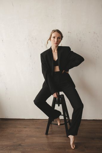 A beautiful young European girl in a black suit posing at the camera while sitting on a stool