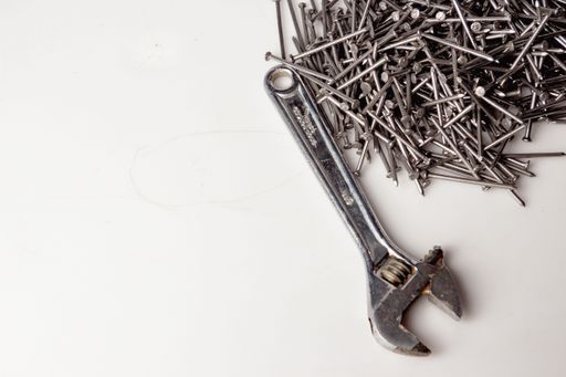 Set of nails piled up on a white work table with a wrench next to it waiting for someone to use them.