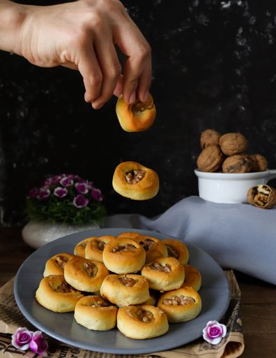 A woman holding freshly baked bread rolls by sprinkling nuts on top