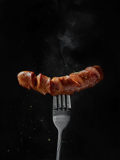 A vertical shot of hot grilled sausage on a fork isolated on black background