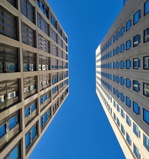 A vertical low angle shot of two modern buildings opposite each other with blue sky in the background